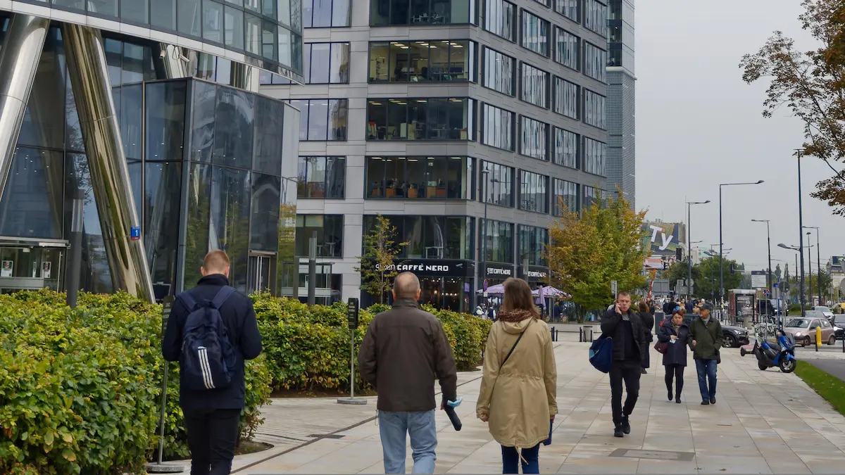 Profissionais caminhando no distrito de Zuidas em Amsterdam, ilustrando o ambiente de trabalho para o visto highly skilled migrant Holanda em 2026, com prédios modernos e bicicletas.